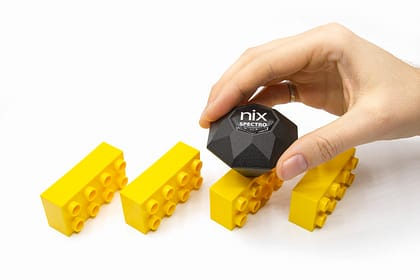 A hand holds the Nix Spectro and scans a yellow building block.