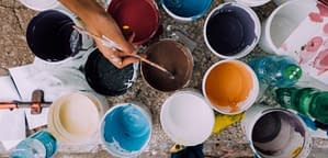 A number of open paint buckets are shown, with a hand dipping a paint brush in the centre can