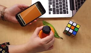 A pair of hands are holding the Nix Mini to an orange to scan, while holding their phone